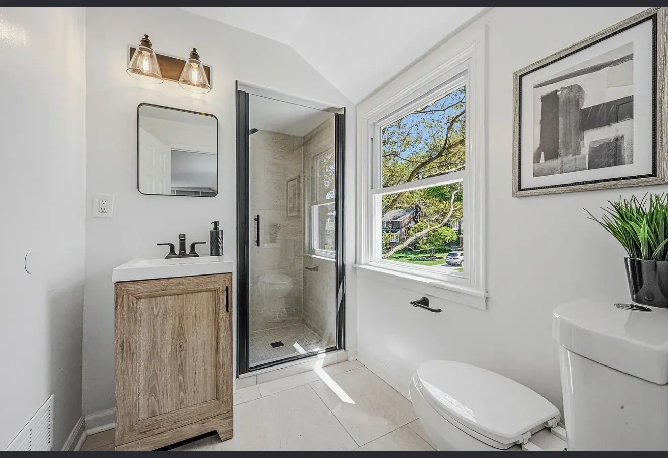 Bright bathroom renovation with walk-in glass shower, oak floating vanity, matte black faucet and natural light from new window — Delaware home remodel