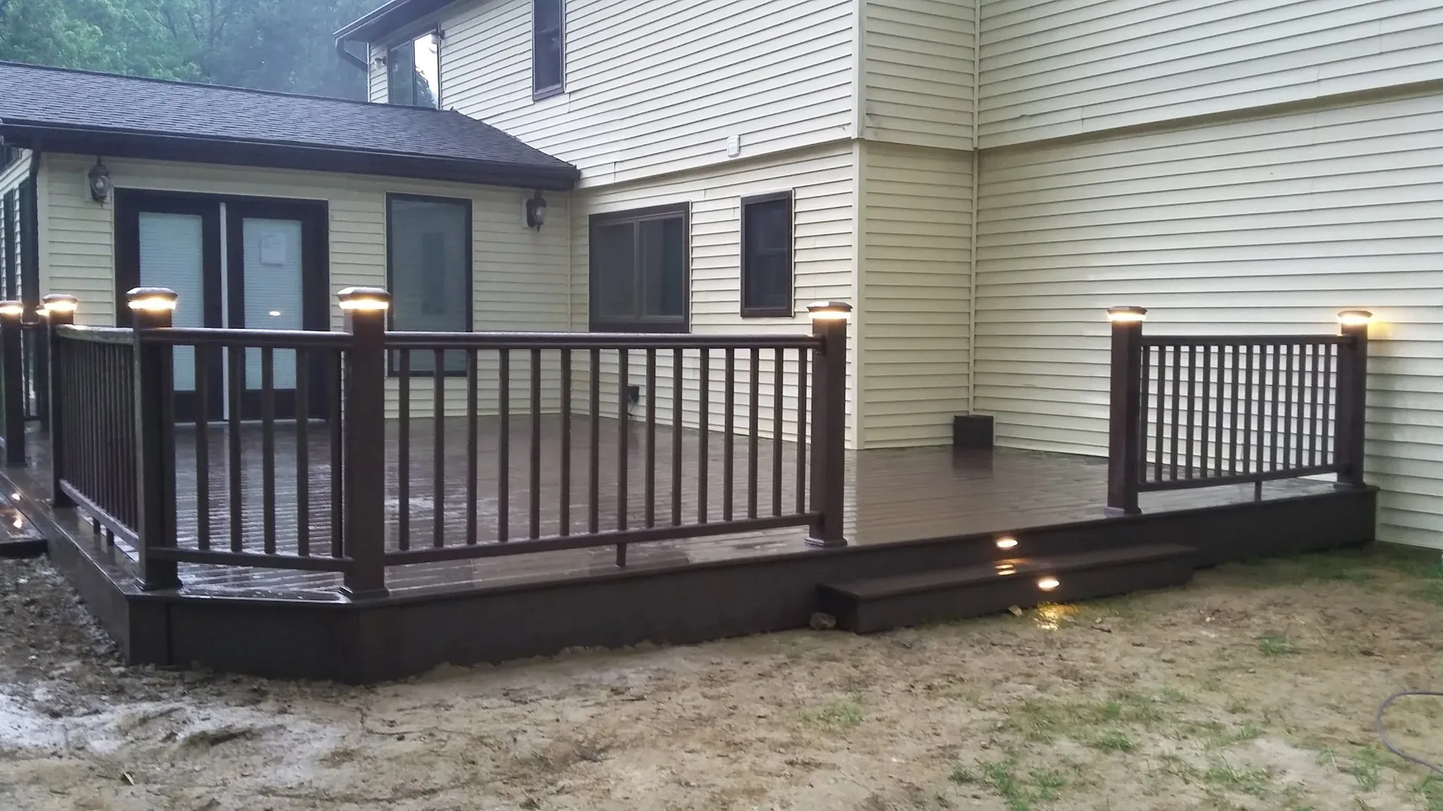 Composite deck at night with low-voltage post-cap lights and recessed step lighting installed by Zavala & Sons