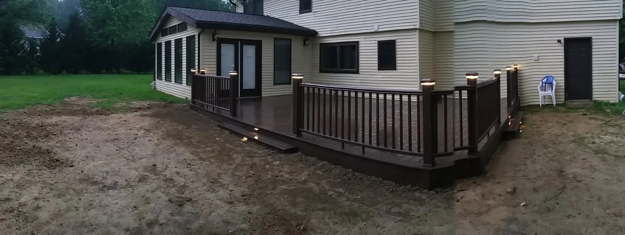 Wraparound composite deck at dusk with integrated post lights and ambient deck lighting — outdoor living build by Zavala & Sons