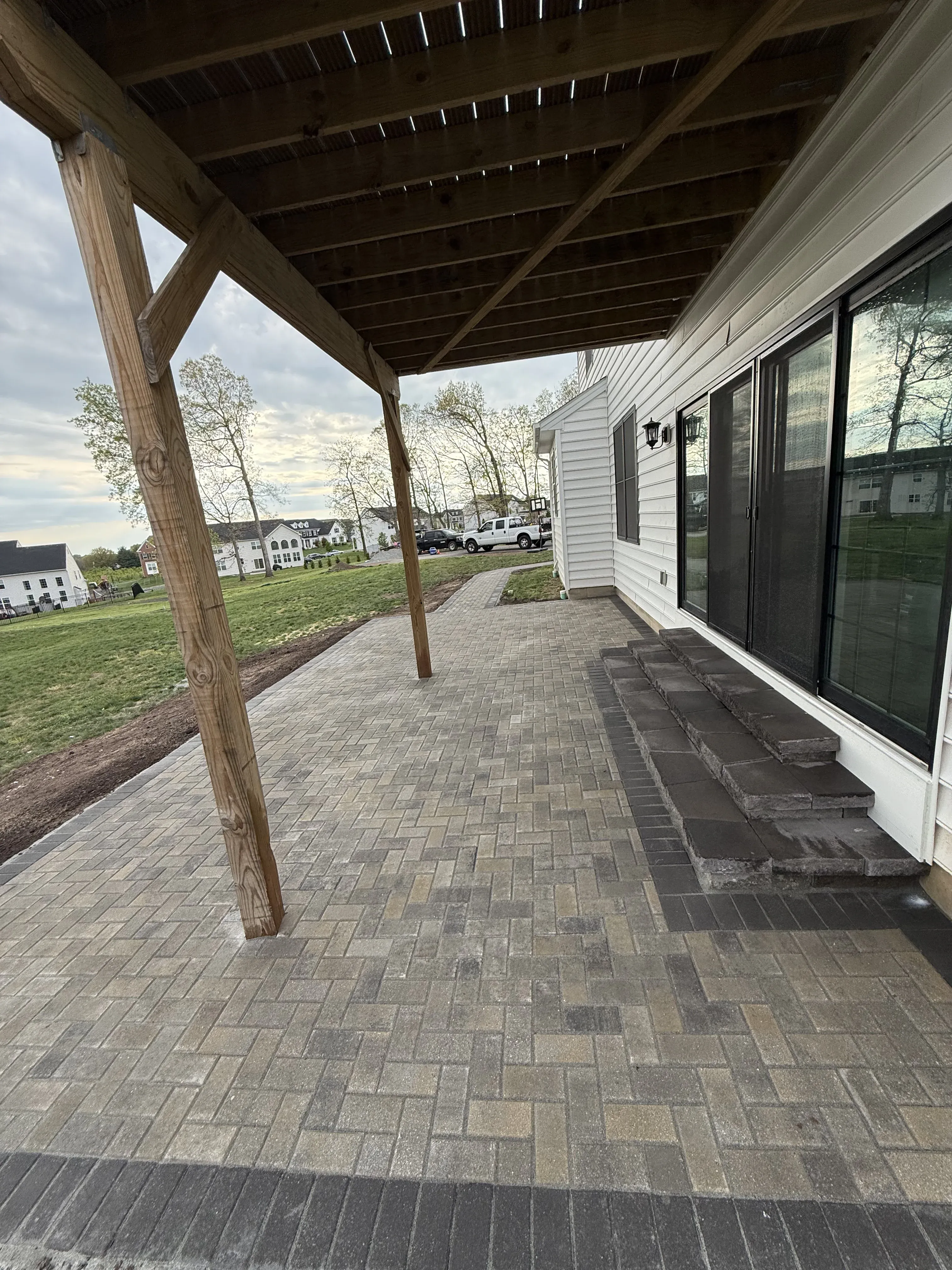 Covered paver patio with wood post pergola roof attached to a Delaware home by Zavala & Sons