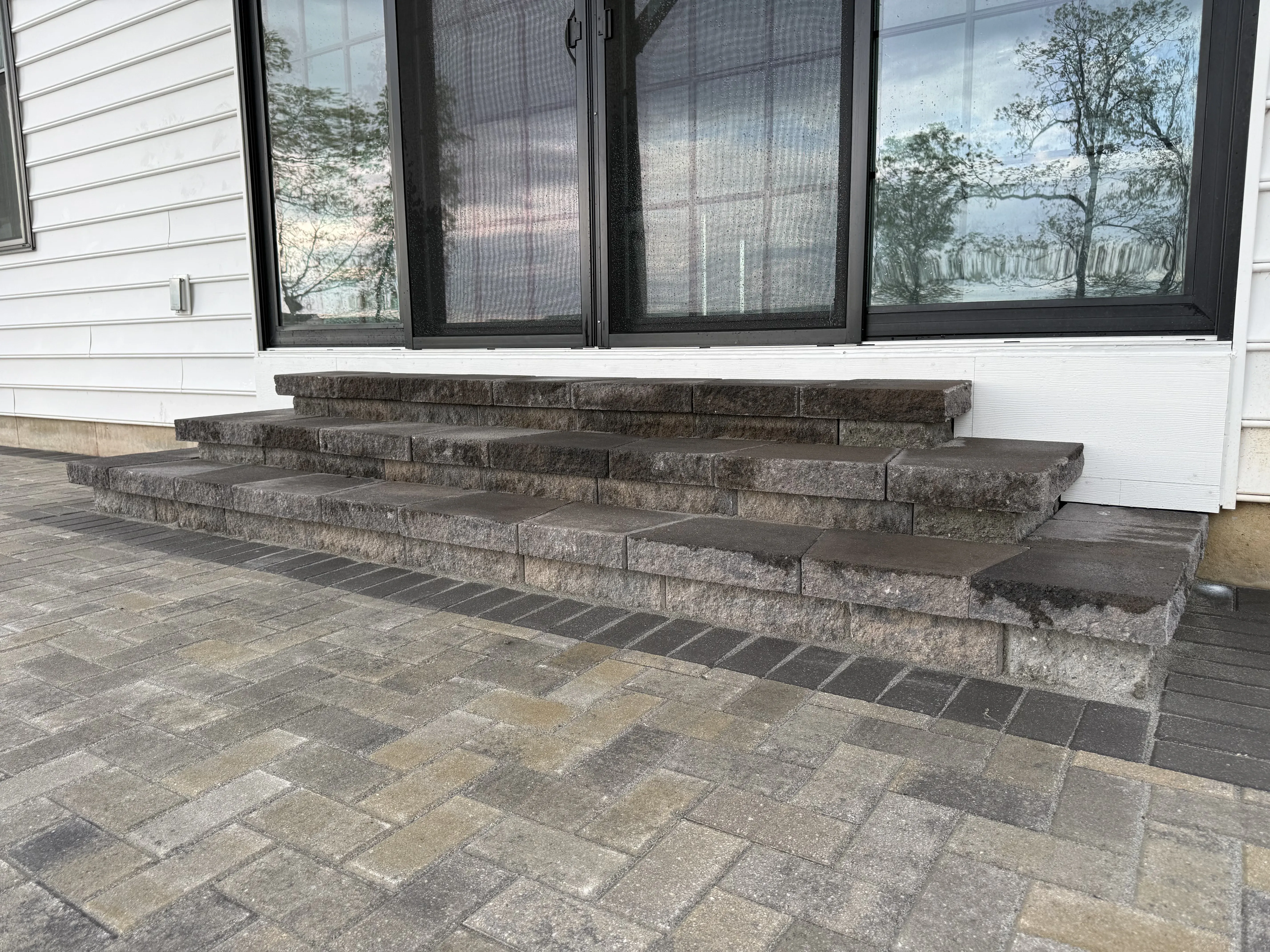Custom stone block raised stairs leading to back patio sliding door with paver patio below — outdoor masonry by Zavala & Sons